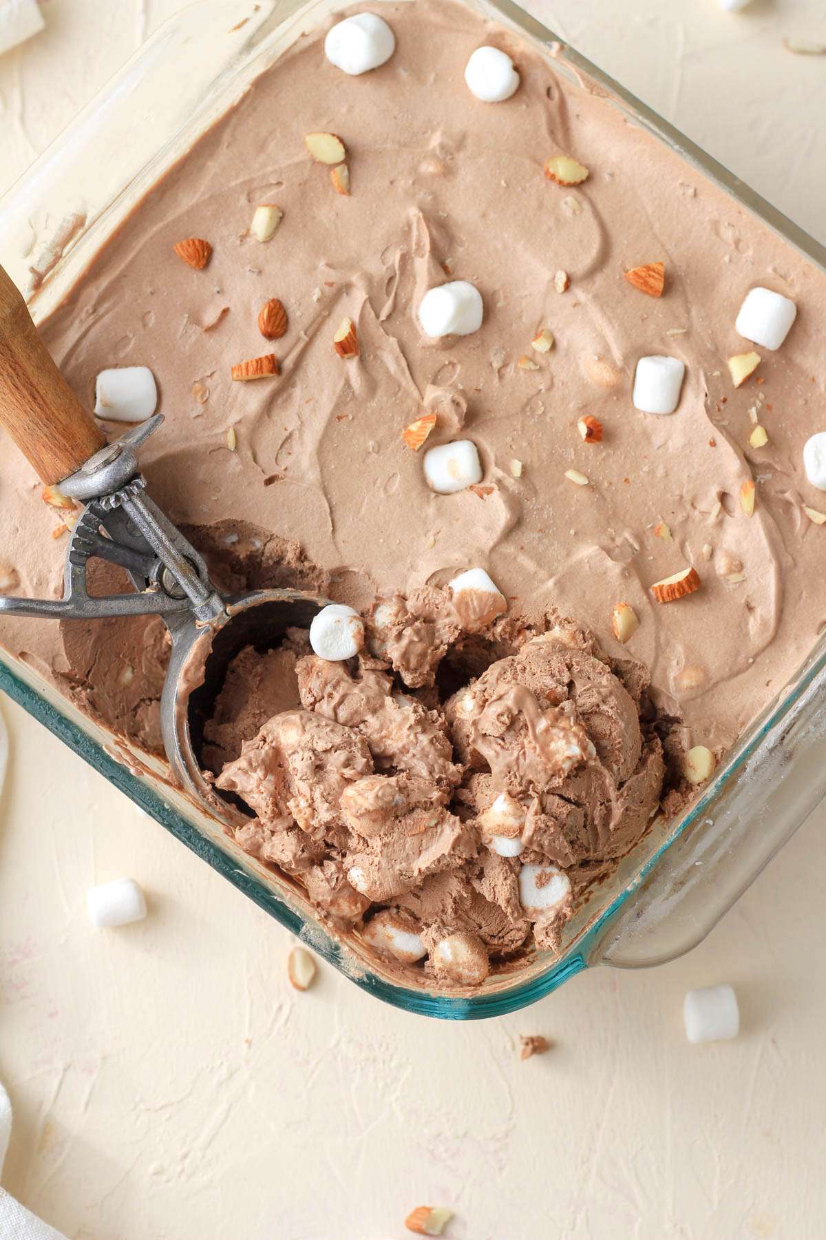 A silver and wooden handled ice cream scoop in a pan of dairy free rocky road ice cream.