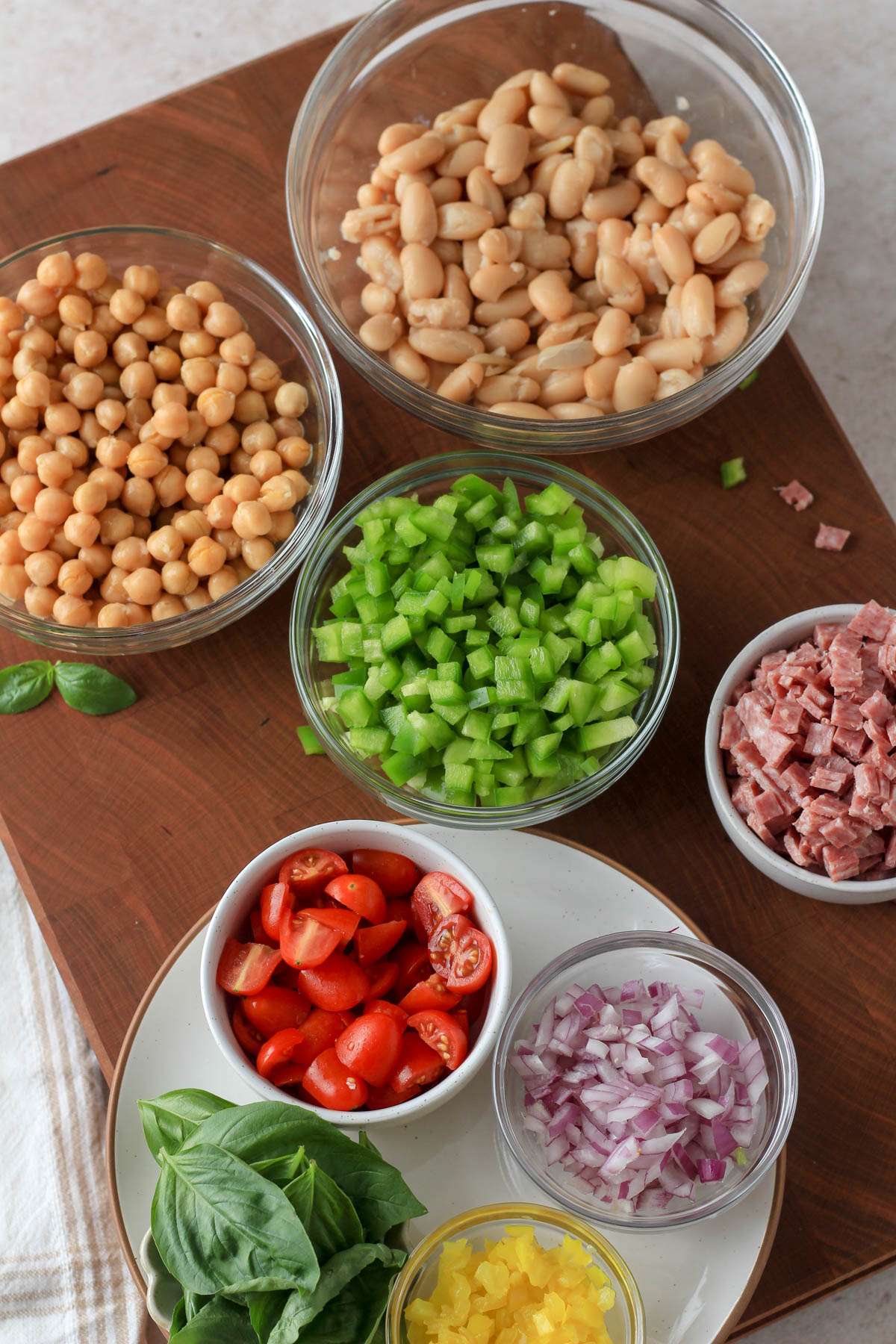 Ingredients for Italian grinder bean salad on a wooden cutting board.