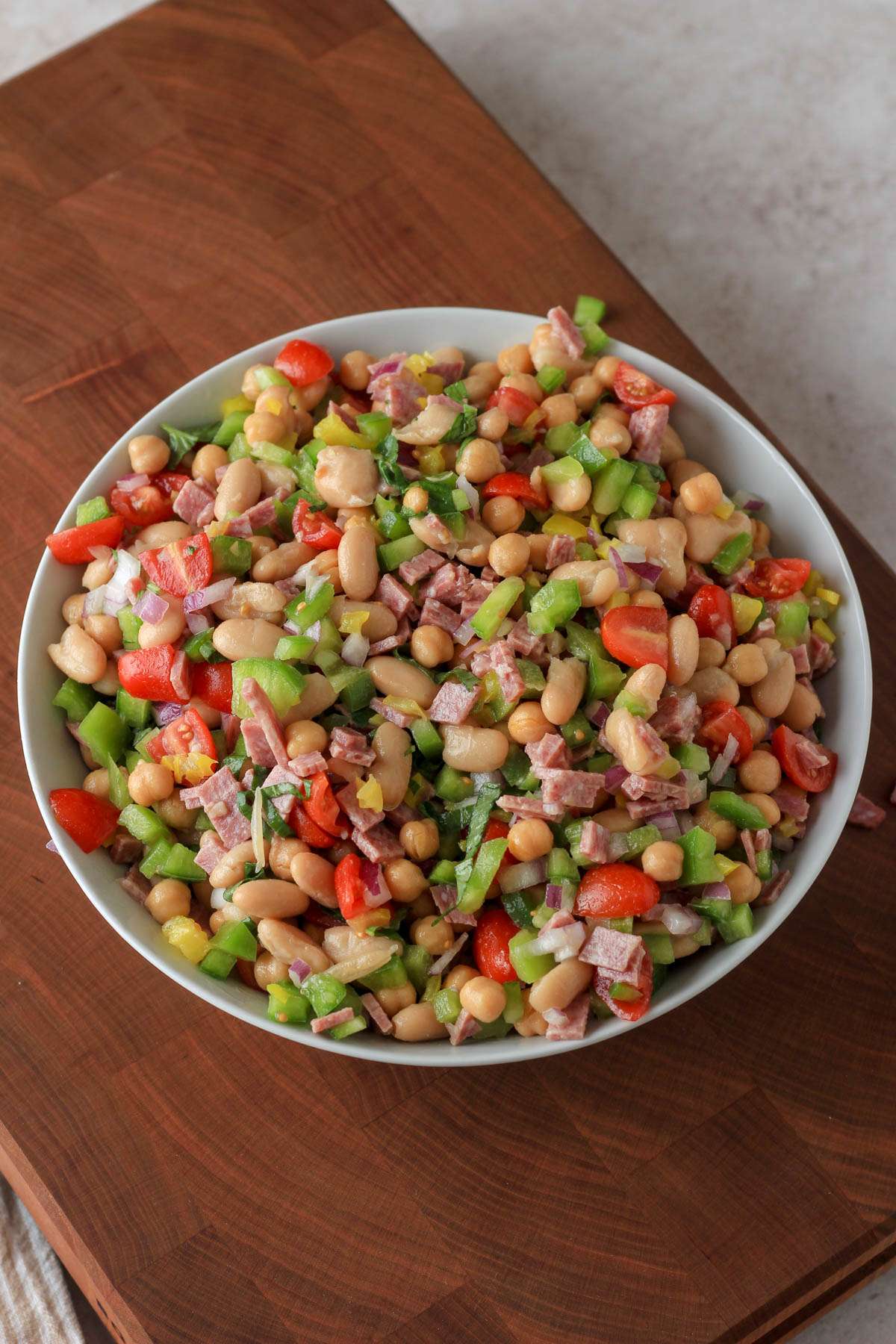 A white bowl of Italian bean salad on a wooden cutting board.