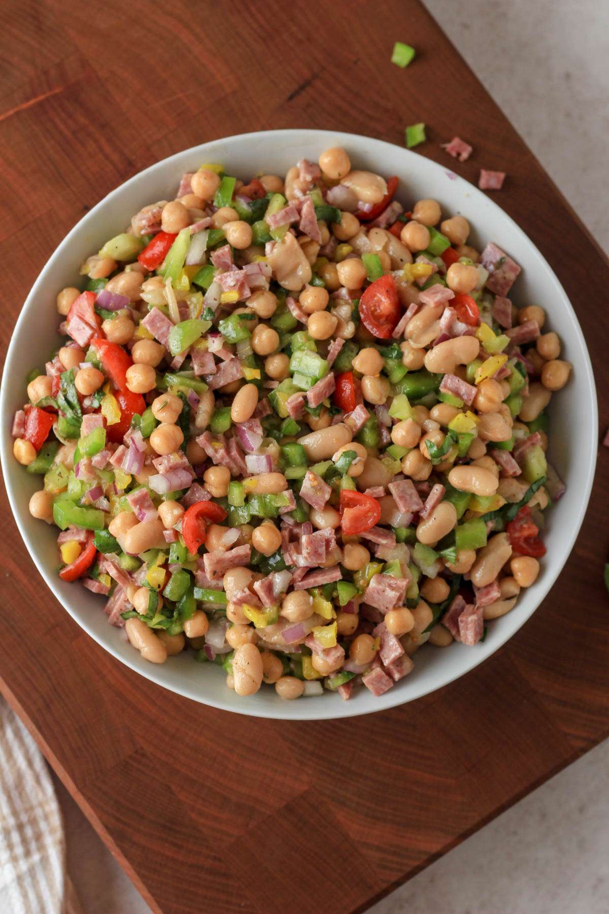 A top down image of a white bowl with Italian grinder bean salad on a wooden cutting board.