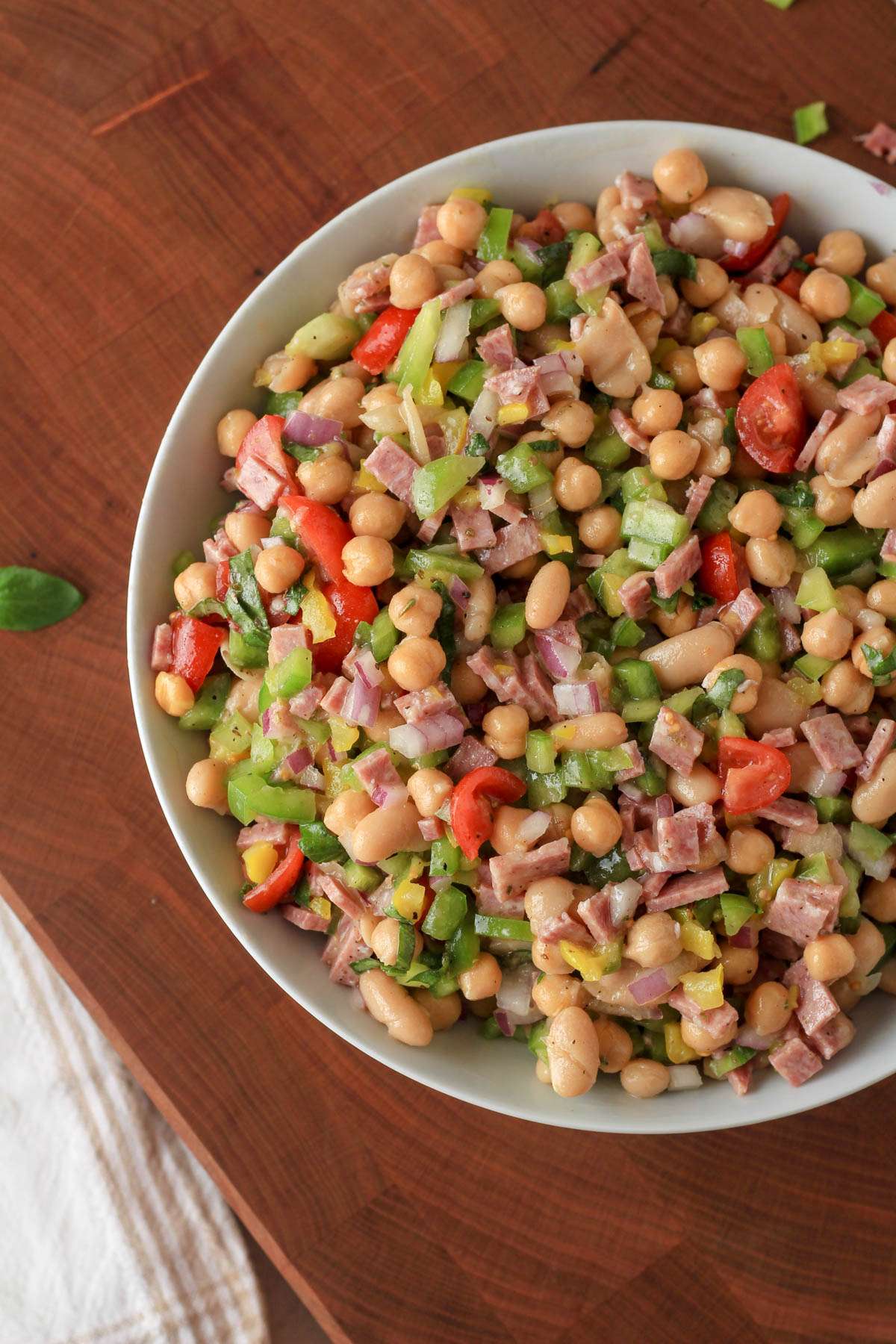 Italian bean salad in a white bowl on a wooden cutting board.