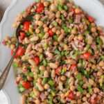 A close up of the top of a white platter with a silver spoon scooping Italian bean salad.