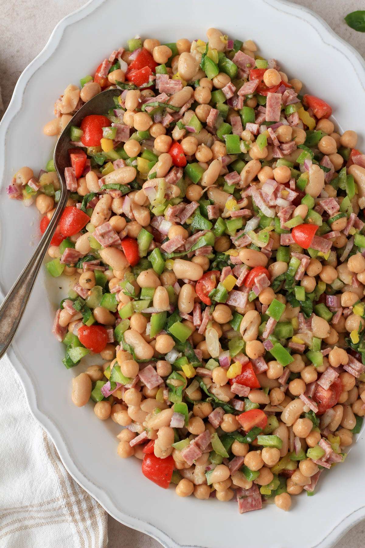 Dairy free Italian grinder bean salad on a white platter with a large silver spoon.