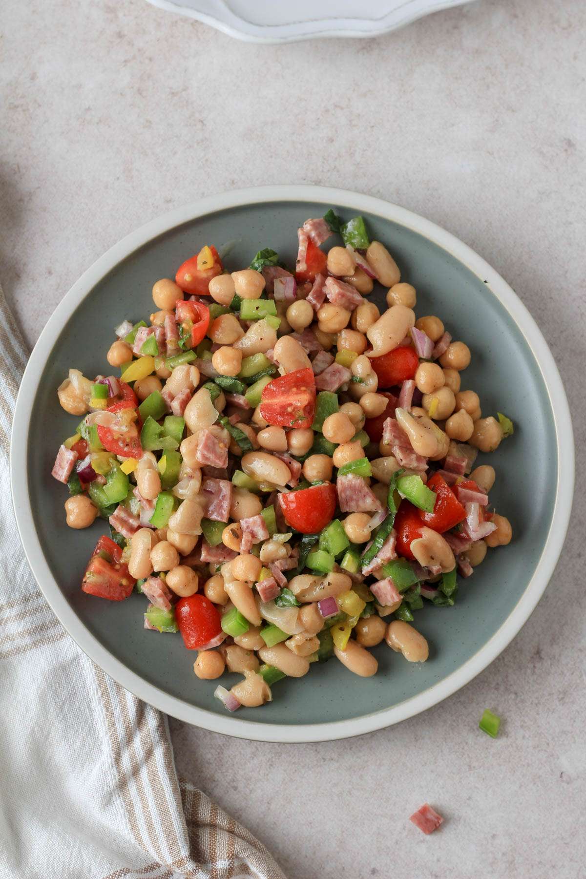 A small green plate on a tan counter with a serving of Italian grinder bean salad on top.