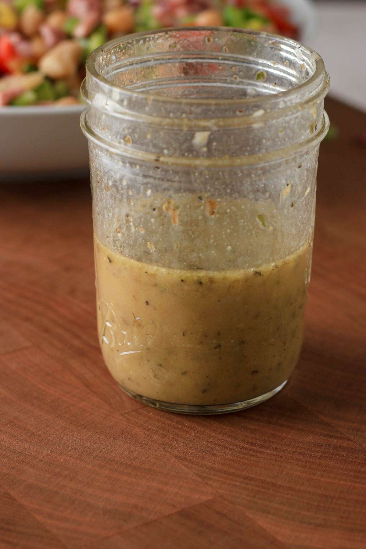 A small mason jar with Italian dressing before topping the grinder inspired bean salad.